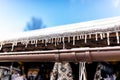 Hanging icicles from the roof of a wooden building on a winter frosty day, a lot of snow on the roof, a visible plastic gutter and Royalty Free Stock Photo