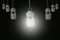 Hanging light bulbs with glowing one on dark background. Royalty Free Stock Photo