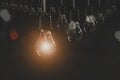 Hanging light bulbs with glowing one on dark background. Royalty Free Stock Photo