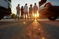 Backs of five young ordinary dressed friends standing next to each other outside on a parking site with their cars on a Royalty Free Stock Photo