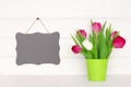 Hanging small black vintage chalkboard on white painted wooden wall near tulip flower bouquet. Spring mockup background Royalty Free Stock Photo