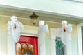 Hanging white ghosts on front porch of home with red door and lamp in suburban setting in the neighborhood Royalty Free Stock Photo