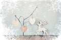 Hanging wooden hearts over and wooden rain deer decoration over wooden background. retro filtered image with snowflake overlay Royalty Free Stock Photo