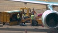 Four male airport employees handling luggage coming out of the big airplane.
