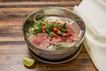 Hanoi rare Beef Pho topping with onion, noodles, green onion, red chilli, lemon and coriander served in bowl isolated on wooden Royalty Free Stock Photo
