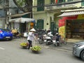 HANOI, VIETNAM - JUNE 28, 2017: a woman carrying fruit using a shoulder pole and two baskets along a street in hanoi