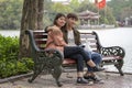 Young Vietnamese couple is sitting on a park bench near the pond in the old town of Hanoi, Vietnam