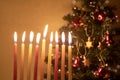 Hanukkah candles burning on the background of Christmas tree, decorated with some snowflakes