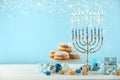 Hanukkah celebration. Menorah with burning candles, dreidels, gift boxes and donuts on white wooden table against light blue Royalty Free Stock Photo