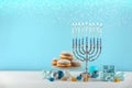 Hanukkah celebration. Menorah with burning candles, dreidels, gift boxes and donuts on white wooden table against light blue Royalty Free Stock Photo