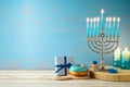 Hanukkah concept with menorah, candles, gift box and traditional donut on wooden table over blue background Royalty Free Stock Photo