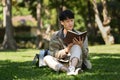 Happ young asian man reading interesting book while while sitting on green grass at sunny beautiful day Royalty Free Stock Photo