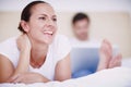 Happily counting her blessings. A young woman lying on a bed while her husband works on a laptop in the background. Royalty Free Stock Photo