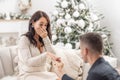 Happily crying woman lets her proposing boyfriend put a ring on her finger during Christmas