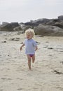 Happily smiling cute little boy running in the sand at a beach, summer holiday feeling, rocks in the background Royalty Free Stock Photo