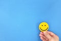 Happiness and be positive concept. Male hand holding yellow smiling face in blue background with copy space. Royalty Free Stock Photo