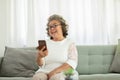 Happiness beautiful elderly asian woman with white hairs sitting on sofa using mobile phone and social media smile at home,Senior Royalty Free Stock Photo