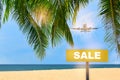 Sale word written on yellow sign and commercial plane flying on blue sky with coconut palm leaves and tropical beach background Royalty Free Stock Photo
