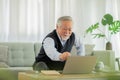 Happiness elderly asian man sitting on sofa and using computer laptop VDO Conference online meeting with family or business team Royalty Free Stock Photo