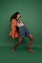 Emotional african girl in shorts and shirt dancing, having fun isolated on dark green background. Concept of beauty, art Royalty Free Stock Photo