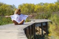 Happiness and freedom. One happy and free woman sitting alone on a wooden pier at the park opening arms and enjoying feeling.