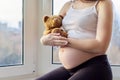 Pregnant young happy woman with toy teddy bear, at home near window Royalty Free Stock Photo