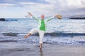 Happiness in senior attractive man standing barefoot on the shoreline while jokingly lifts one leg. Mature man holding shoes and Royalty Free Stock Photo