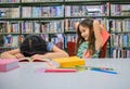 Happiness two cute diversity girls reading book and teasing to hit sleeping friend in school library funny. People lifestyle and Royalty Free Stock Photo