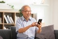 Happiness of wellness elderly asian man with white hairs sitting on sofa using mobile phone and social media smile at home. Royalty Free Stock Photo