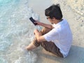 Happiness young Asian man with mobile smart phone sitting on sand of tropical beach. Summer vacations concept. Internet of things Royalty Free Stock Photo