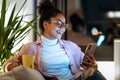 Happiness young entrepreneur woman using her smart phone while drinking a cup of coffee sitting on couch in the office Royalty Free Stock Photo