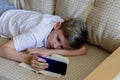 Teen boy is using phone with open book lying on the sofa.