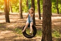 Happy active child girl playing on swing wheel in forest on sunny summer day. Preschool child having fun and swinging on a tire Royalty Free Stock Photo