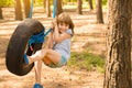 Happy active child girl playing on swing wheel in forest on sunny summer day. Preschool child having fun and swinging on a tire Royalty Free Stock Photo