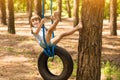 Happy active child girl playing on swing wheel in forest on sunny summer day. Preschool child having fun and swinging on a tire Royalty Free Stock Photo