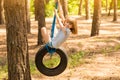 Happy active child girl playing on swing wheel in forest on sunny summer day. Preschool child having fun and swinging on a tire Royalty Free Stock Photo