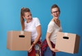 Happy active hipster roommates holding cardboard boxes on blue