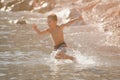 Happy active little delightful boy in sport shorts running in sea water with splash on summer sunny beach Royalty Free Stock Photo