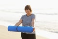 Happy active middle aged woman in sport wear showing yoga mat on sunrise in the morning on seashore beach on summer day Royalty Free Stock Photo