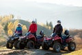 Happy active riders in protective helmets enjoying extreme riding on ATV quad motorbikes in fall mountains at sunset