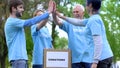 Happy activists putting clothes donation box and giving high five, volunteering