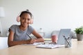 Happy adolescent afro american schoolgirl with headphones study at home with laptop prepare for test and exam Royalty Free Stock Photo