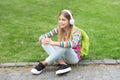 Happy adolescent girl with backpack listening to music sitting on grass outdoors, education Royalty Free Stock Photo