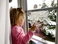 Happy adorable baby girl sitting near window and looking outside on snow on Christmas day or morning. Smiling healthy Royalty Free Stock Photo