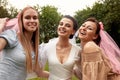 Happy adorable bride in a white dress with a white veil and two bridesmaids in a blue and beige dress with pink veils