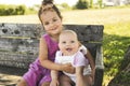 Happy adorable chubby baby girl sitting on a bench with her daughter sister