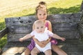 Happy adorable chubby baby girl sitting on a bench with her daughter sister