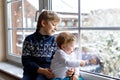 Happy adorable kid boy and cute baby girl sitting near window and looking outside on snow on Christmas day or morning Royalty Free Stock Photo