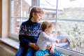 Happy adorable kid boy and cute baby girl sitting near window and looking outside on snow on Christmas day or morning Royalty Free Stock Photo