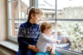 Happy adorable kid boy and cute baby girl sitting near window and looking outside on snow on Christmas day or morning Royalty Free Stock Photo